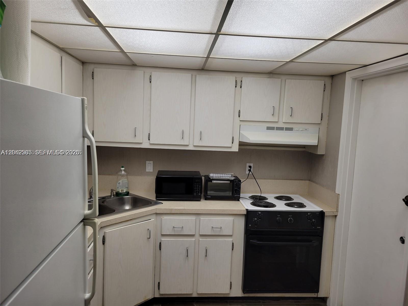 A small kitchen features white cabinets, a black stove, a microwave, and a drop ceiling — 4200 NW 3rd Ct # 224, Plantation FL 33317, PLANTATION, FL