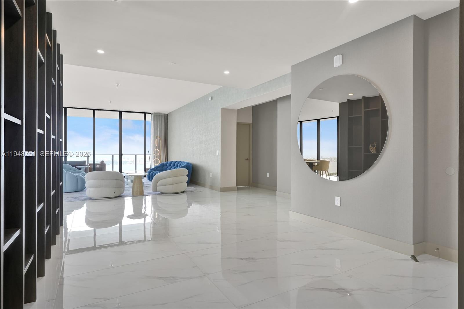 A spacious living area features white marble floors, a large circular mirror, and floor-to-ceiling windows — 700 NE 24, Miami FL 33137, MIAMI, FL