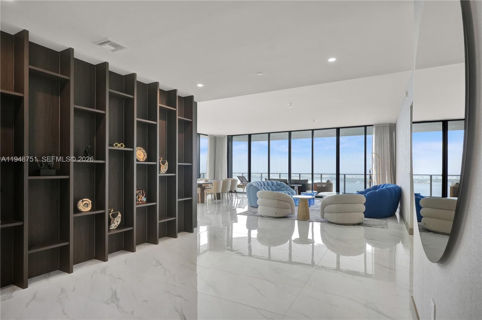 A modern living room features a dark wood shelving unit, marble floors, and floor-to-ceiling windows — 700 NE 24, Miami FL 33137, MIAMI, FL