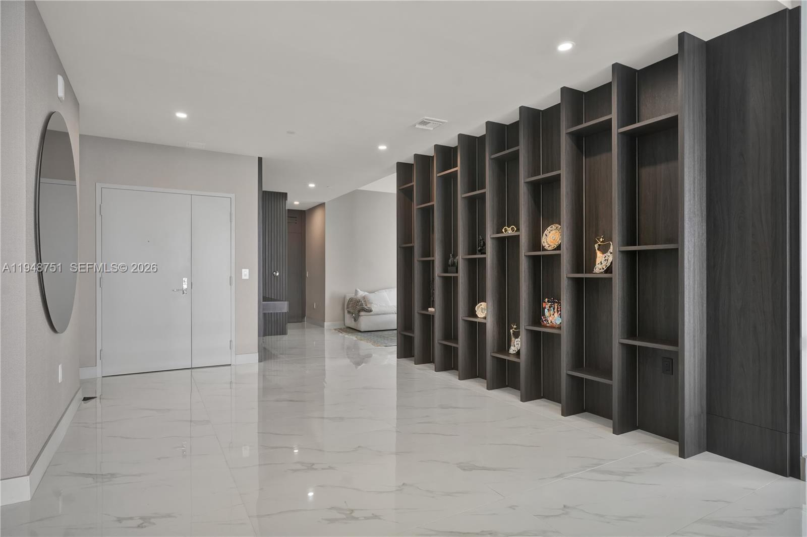 A modern entryway features white marble floors, a large oval mirror, and dark wood shelving — 700 NE 24, Miami FL 33137, MIAMI, FL