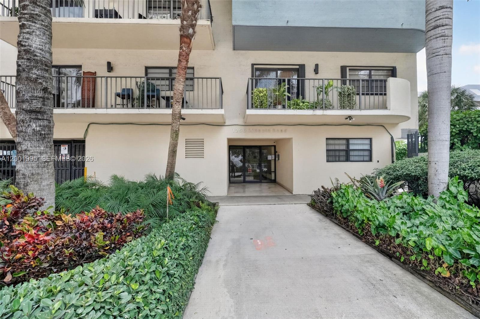 The exterior of a multi-story apartment building features balconies, a glass entrance, and lush landscaping — 1250 Lincoln Rd # 404, Miami Beach FL 33139, MIAMI BEACH, FL