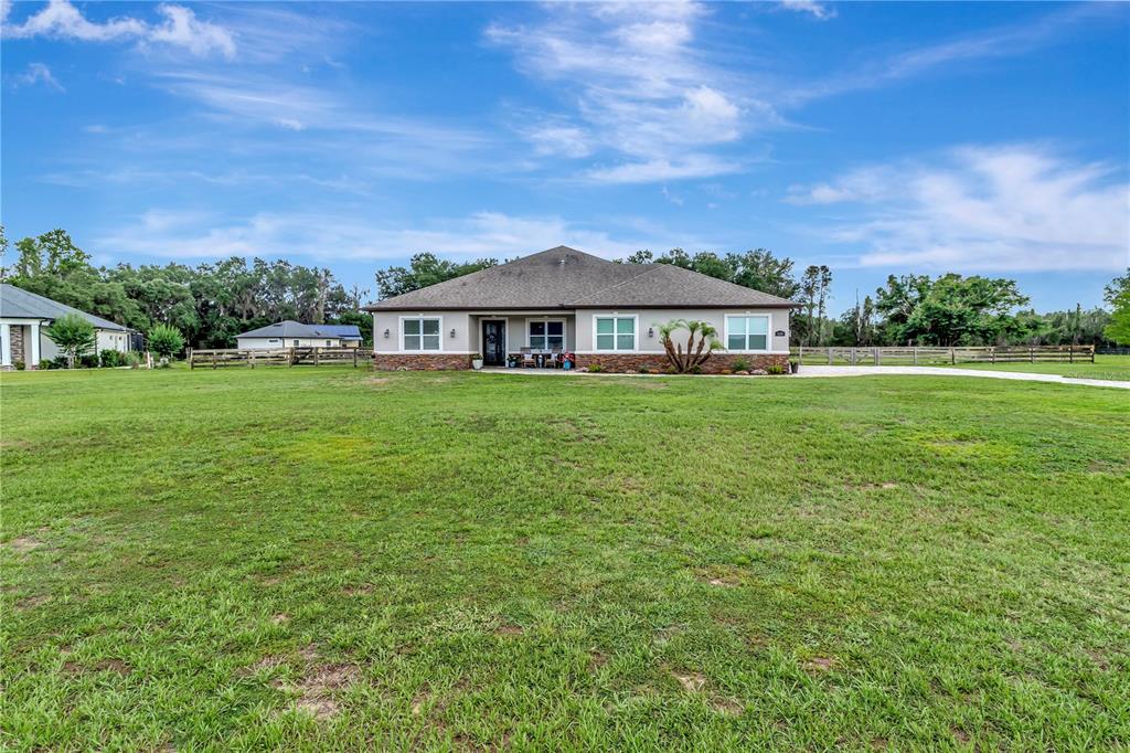 A single-story house with a stone facade sits on a large, grassy rural lot — 5020 LAKESHORE RANCH ROAD, GROVELAND, FL