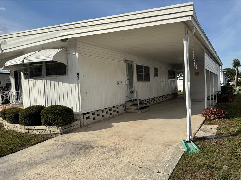 A white mobile home features a concrete driveway, a carport, and a small landscaped garden — 2331 BELLEAIR ROAD UNIT 804, CLEARWATER, FL