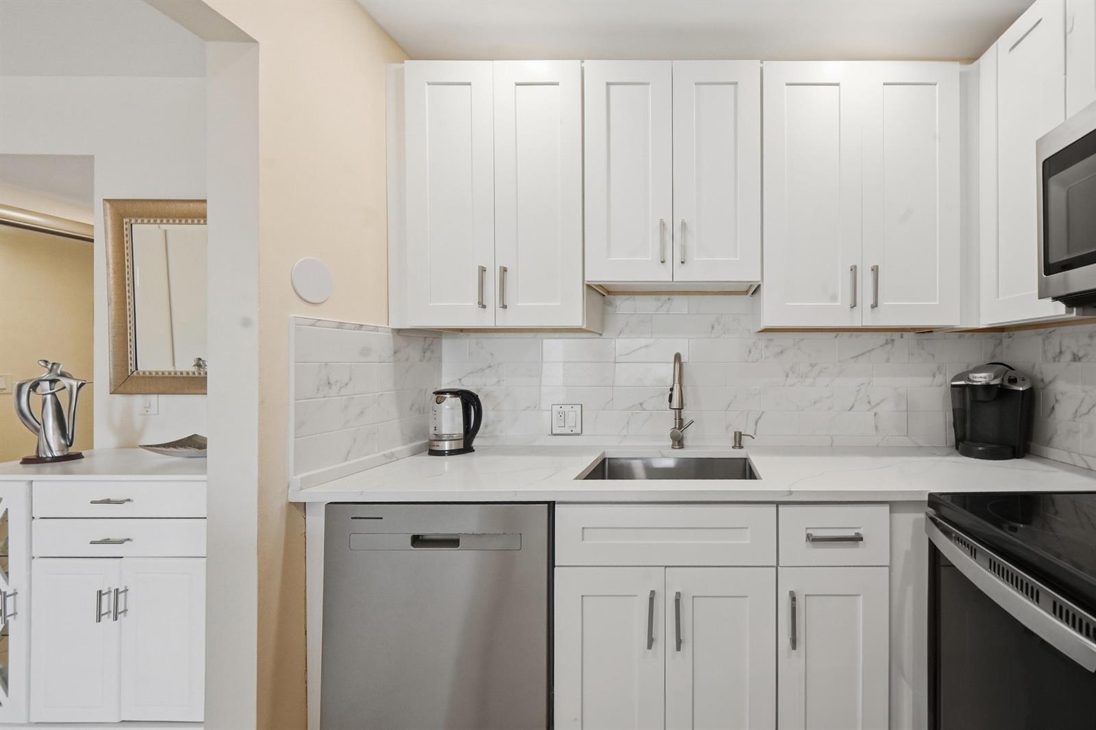 A kitchen features white cabinets, stainless steel appliances, a marble-look backsplash, and quartz countertops — 314 Brighton # H, Boca Raton FL 33434, BOCA RATON, FL