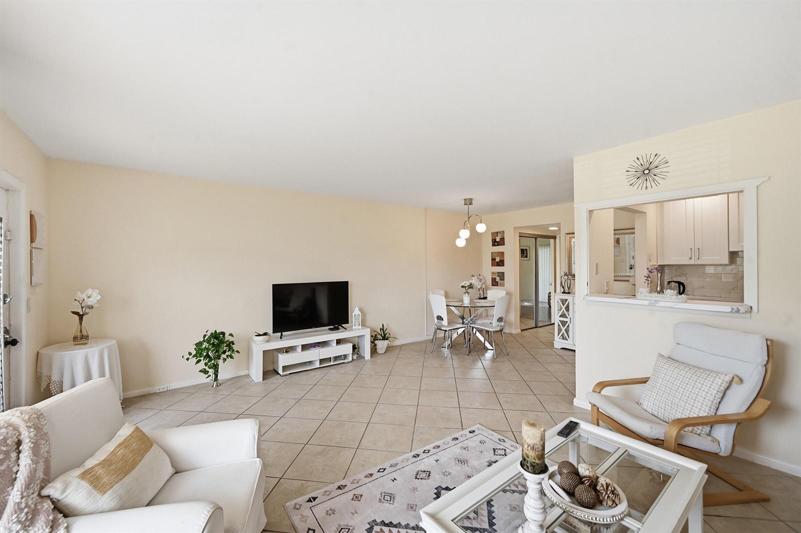 A living room with tile flooring, a white media console, and an open kitchen pass-through — 314 Brighton # H, Boca Raton FL 33434, BOCA RATON, FL