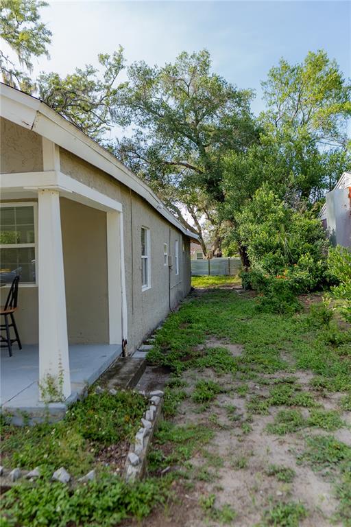 A side view of a house exterior with a covered porch and a grassy yard — 1906 E CARACAS STREET, TAMPA, FL