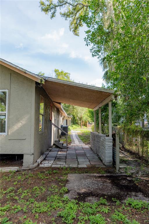 A side view of a house with a covered patio, stone wall, and paved walkway — 1906 E CARACAS STREET, TAMPA, FL