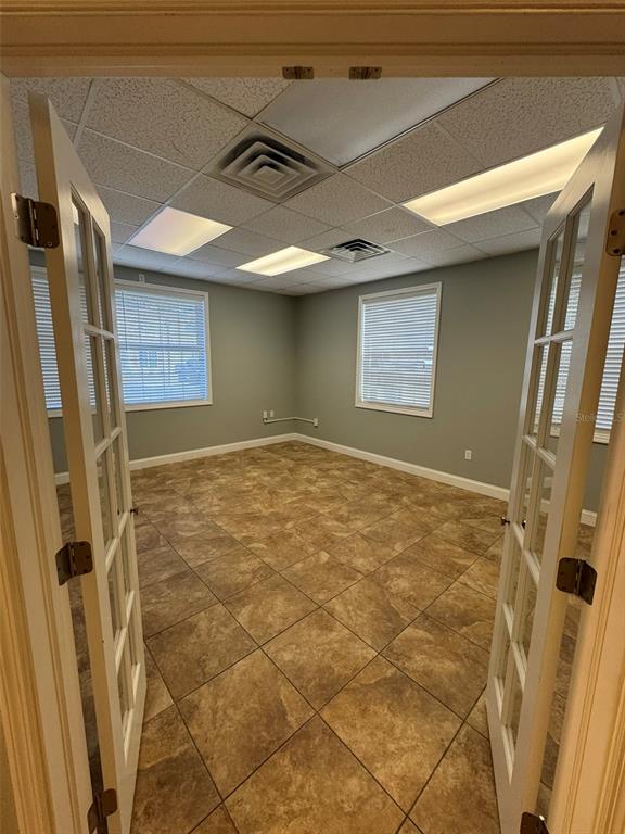 An empty office room features light gray walls, tiled flooring, and two windows with blinds — 2401 W BAY DRIVE UNIT 601, LARGO, FL