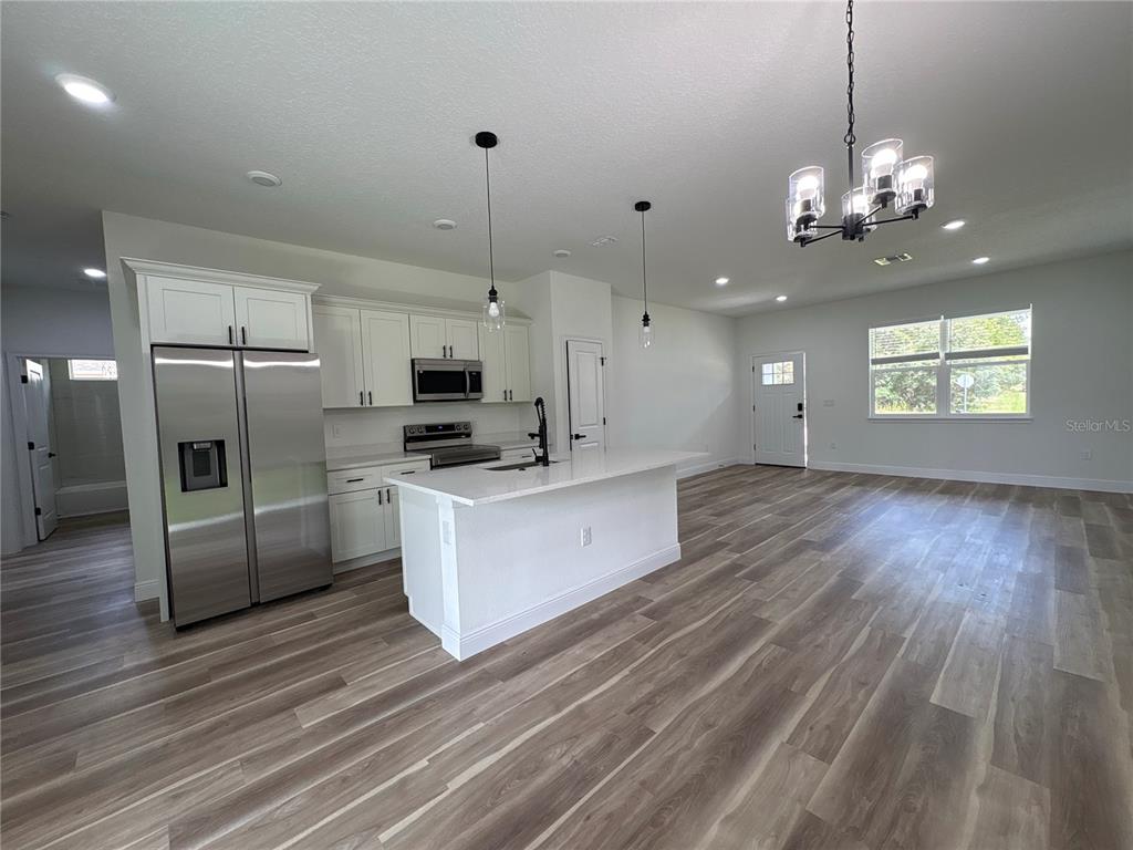 A modern kitchen features white cabinets, stainless steel appliances, a center island, and wood-look flooring — 1852 W QUAKER LANE, CITRUS SPRINGS, FL