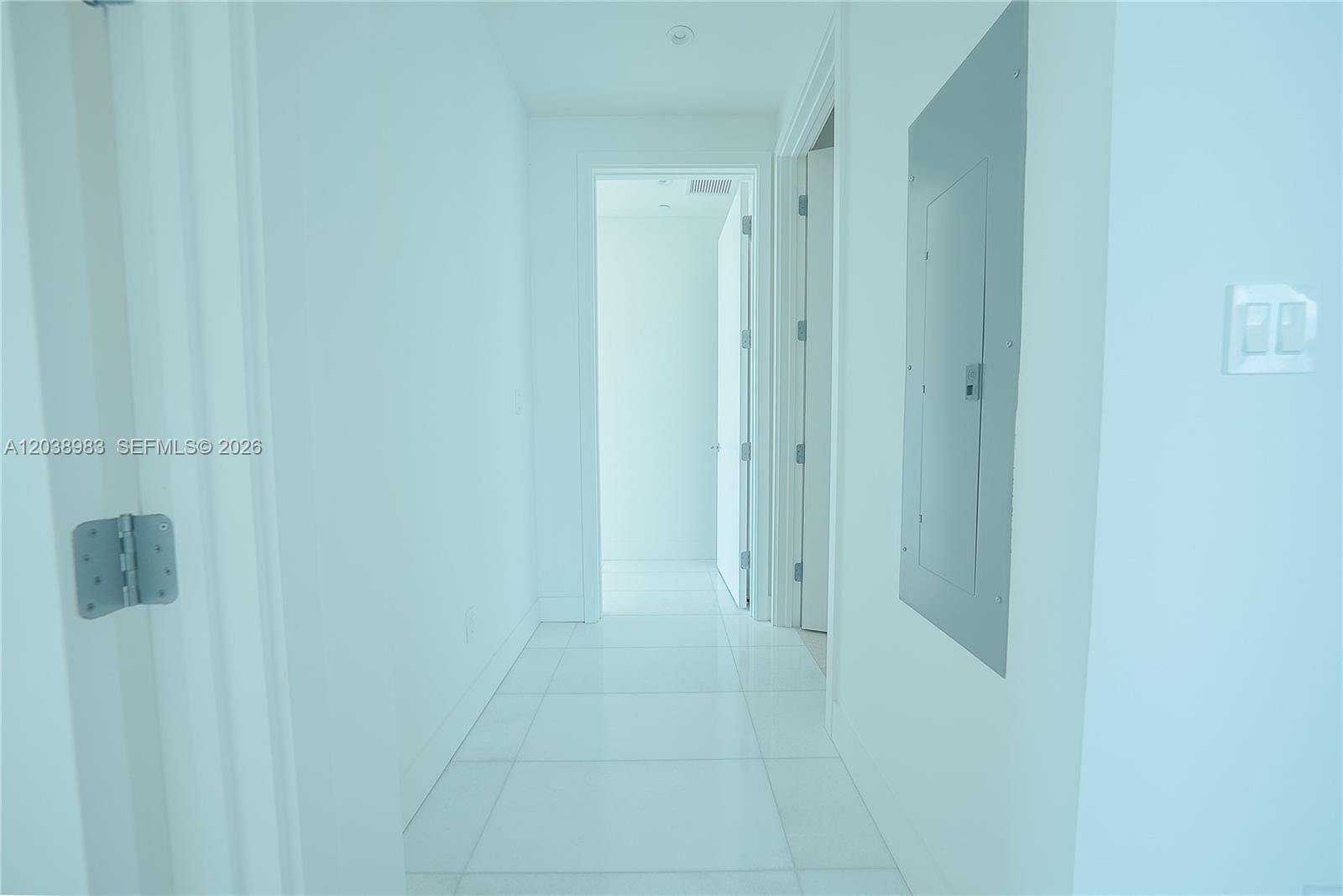 A bright hallway features white tile flooring, white walls, and a gray electrical panel — 175 SE 25th Rd # 2703, Miami FL 33129, MIAMI, FL