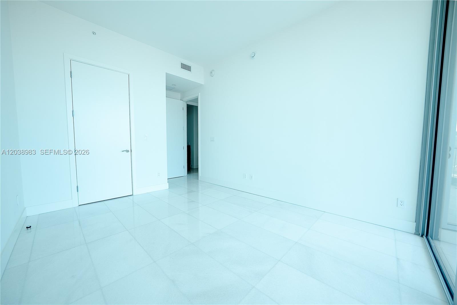 A bright, empty room features white walls, glossy tile flooring, and a sliding glass door — 175 SE 25th Rd # 2703, Miami FL 33129, MIAMI, FL