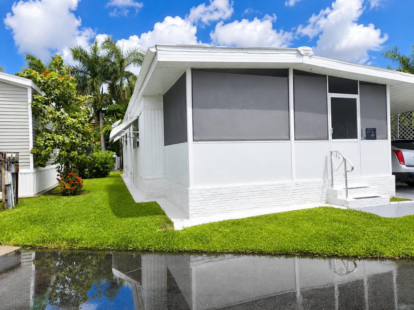 A white manufactured home features a screened-in porch, brick-patterned skirting, and a grassy lawn — 3302 Lake Street, Hollywood FL 33021, HOLLYWOOD, FL