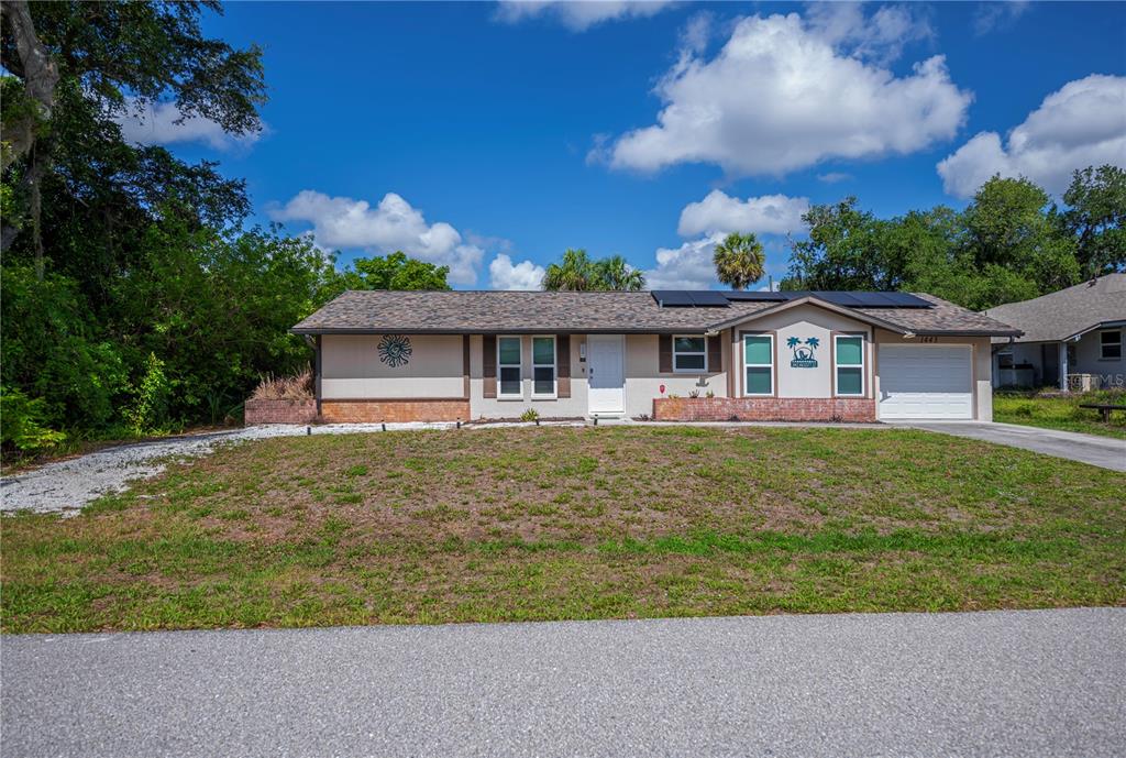 A single-story house with a white garage, brick accents, and solar panels on the roof — 1443 ABSCOTT STREET, PORT CHARLOTTE, FL