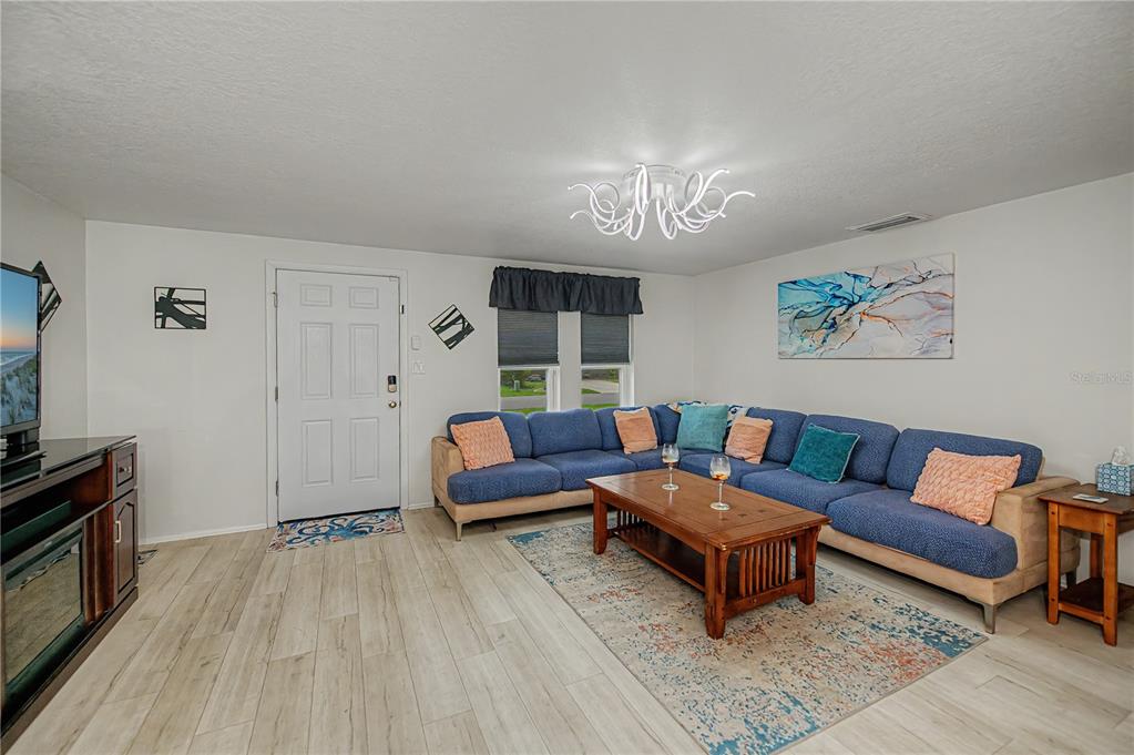 A living room features a blue sectional sofa, a wooden coffee table, and light wood flooring — 1443 ABSCOTT STREET, PORT CHARLOTTE, FL
