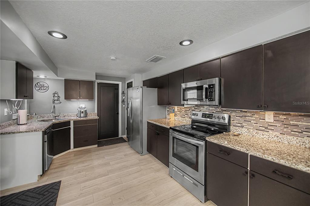 A kitchen features dark brown cabinets, granite countertops, stainless steel appliances, and light wood flooring — 1443 ABSCOTT STREET, PORT CHARLOTTE, FL