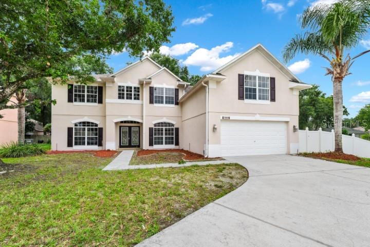 A two-story beige house with a two-car garage, dark shutters, and a concrete driveway — 1889 POMEGRANATE COURT, OCOEE, FL