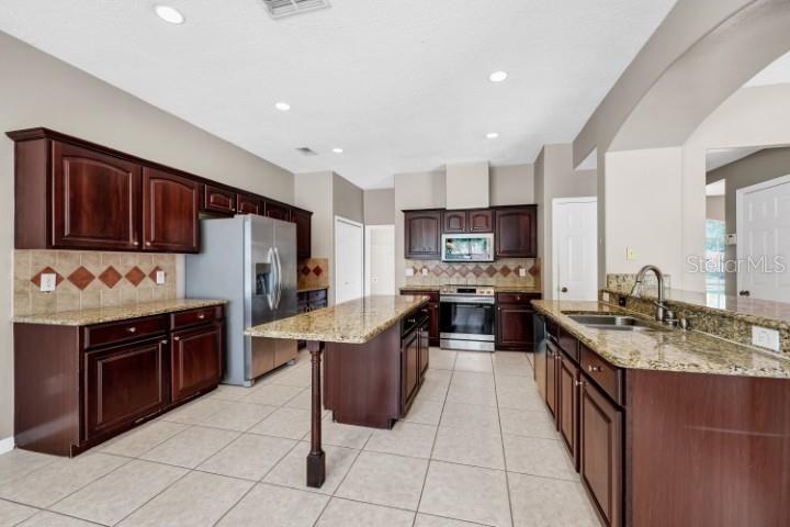 A kitchen features dark wood cabinets, granite countertops, a center island, and stainless steel appliances — 1889 POMEGRANATE COURT, OCOEE, FL