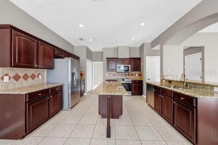 A kitchen features dark wood cabinets, granite countertops, a center island, and stainless steel appliances — 1889 POMEGRANATE COURT, OCOEE, FL