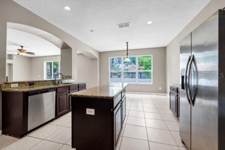 A kitchen features dark wood cabinets, granite countertops, stainless steel appliances, and tile flooring — 1889 POMEGRANATE COURT, OCOEE, FL