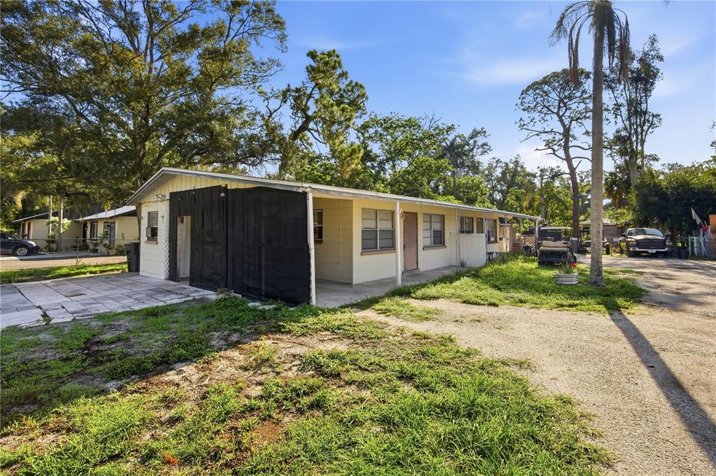 A single-story house with a covered porch and black privacy screens on a gravel lot — 5801 11TH STREET COURT E, BRADENTON, FL