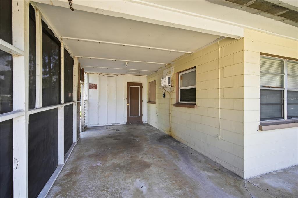A covered concrete patio area features a screen enclosure, a door, and yellow block walls — 5801 11TH STREET COURT E, BRADENTON, FL