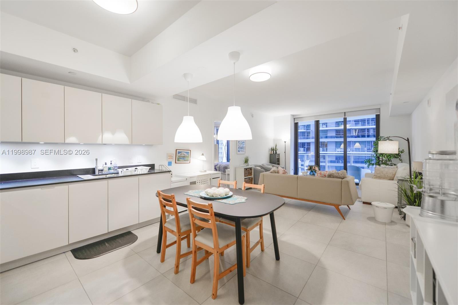 A modern open-concept kitchen and living area features white cabinetry, a dining table, and balcony — 1010 Brickell Ave # 2906, Miami FL 33131, MIAMI, FL