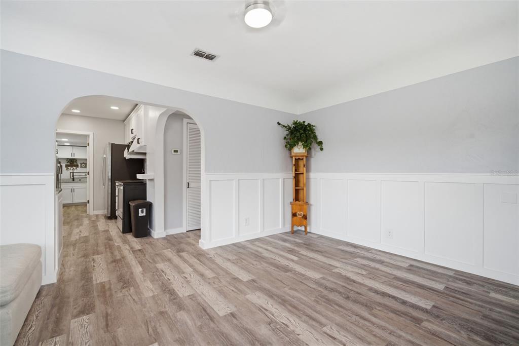 A dining room with white wainscoting, light gray walls, and wood-look flooring leads to a kitchen — 4120 BURLINGTON AVENUE N, ST PETERSBURG, FL