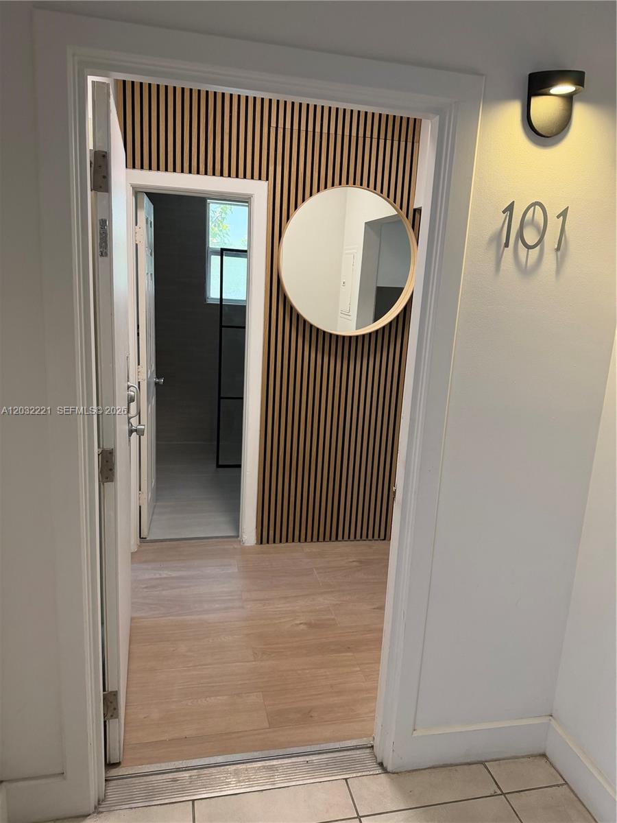 An entryway features wood-slat wall paneling, a round mirror, and a view into a bathroom — 7734 Abbott Ave # 101, Miami Beach FL 33141, MIAMI BEACH, FL