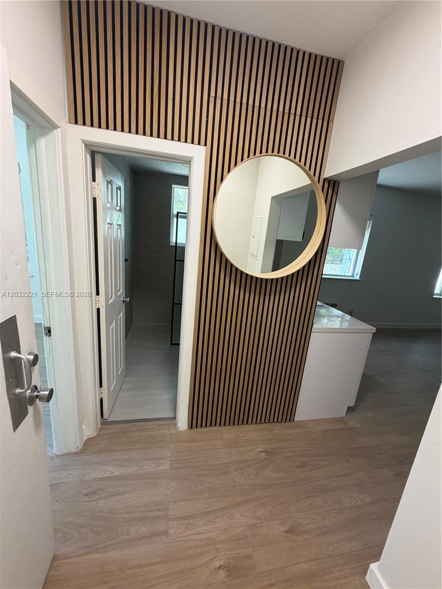 A hallway features wood slat wall paneling, a round mirror, and light wood-look flooring — 7734 Abbott Ave # 101, Miami Beach FL 33141, MIAMI BEACH, FL