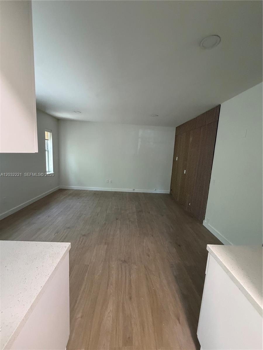 An empty room features light wood-look flooring, white walls, and a wood-slat accent wall — 7734 Abbott Ave # 101, Miami Beach FL 33141, MIAMI BEACH, FL