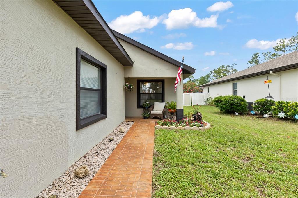A tan house exterior features a brick walkway leading to a covered front porch area — 12 EMMONS LANE, PALM COAST, FL