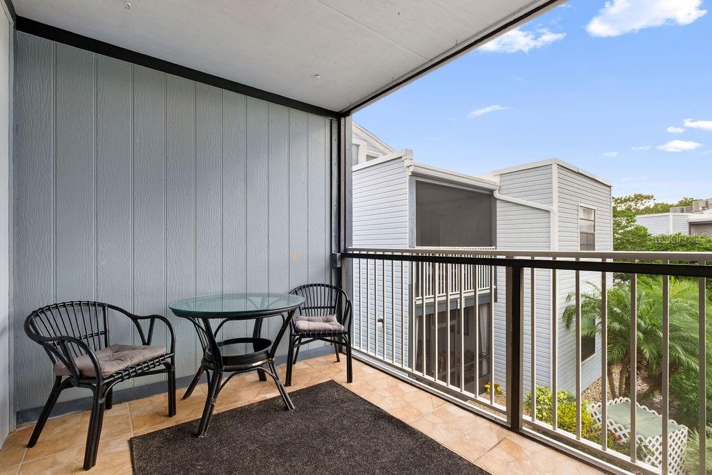A balcony with a glass-topped table, two chairs, and a metal railing overlooks neighboring buildings — 3998 ATRIUM DRIVE UNIT U-1, ORLANDO, FL