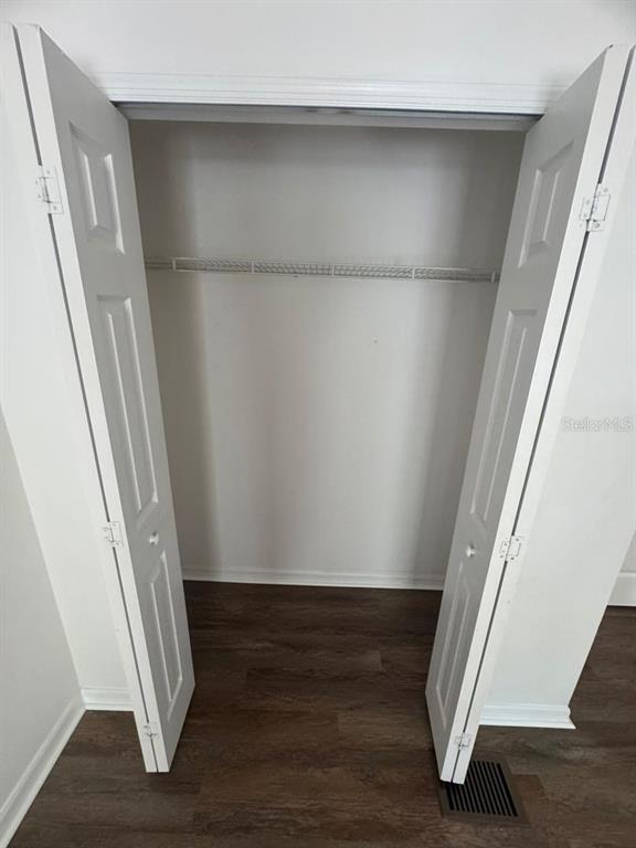 A closet with white bifold doors, a wire shelf, and dark wood-look flooring — 2720 MERRIEWEATHER LANE, KISSIMMEE, FL