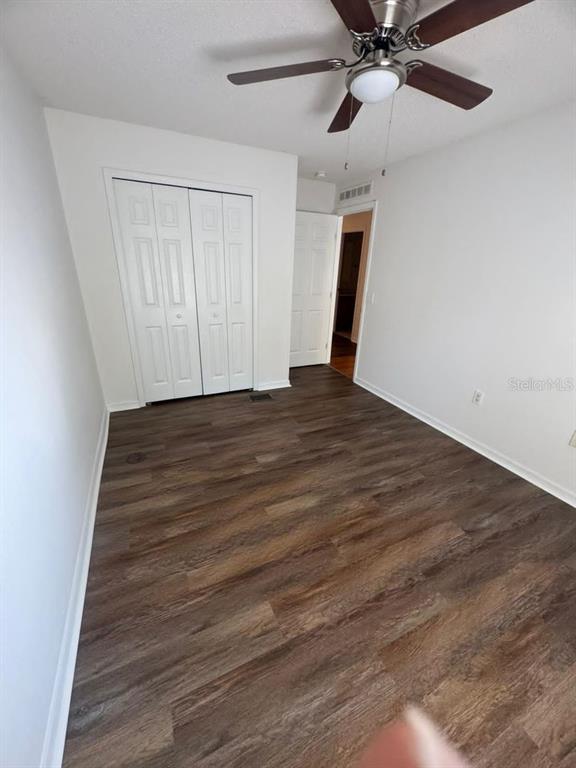 A bedroom with white walls, a ceiling fan, a closet, and dark wood-look flooring — 2720 MERRIEWEATHER LANE, KISSIMMEE, FL