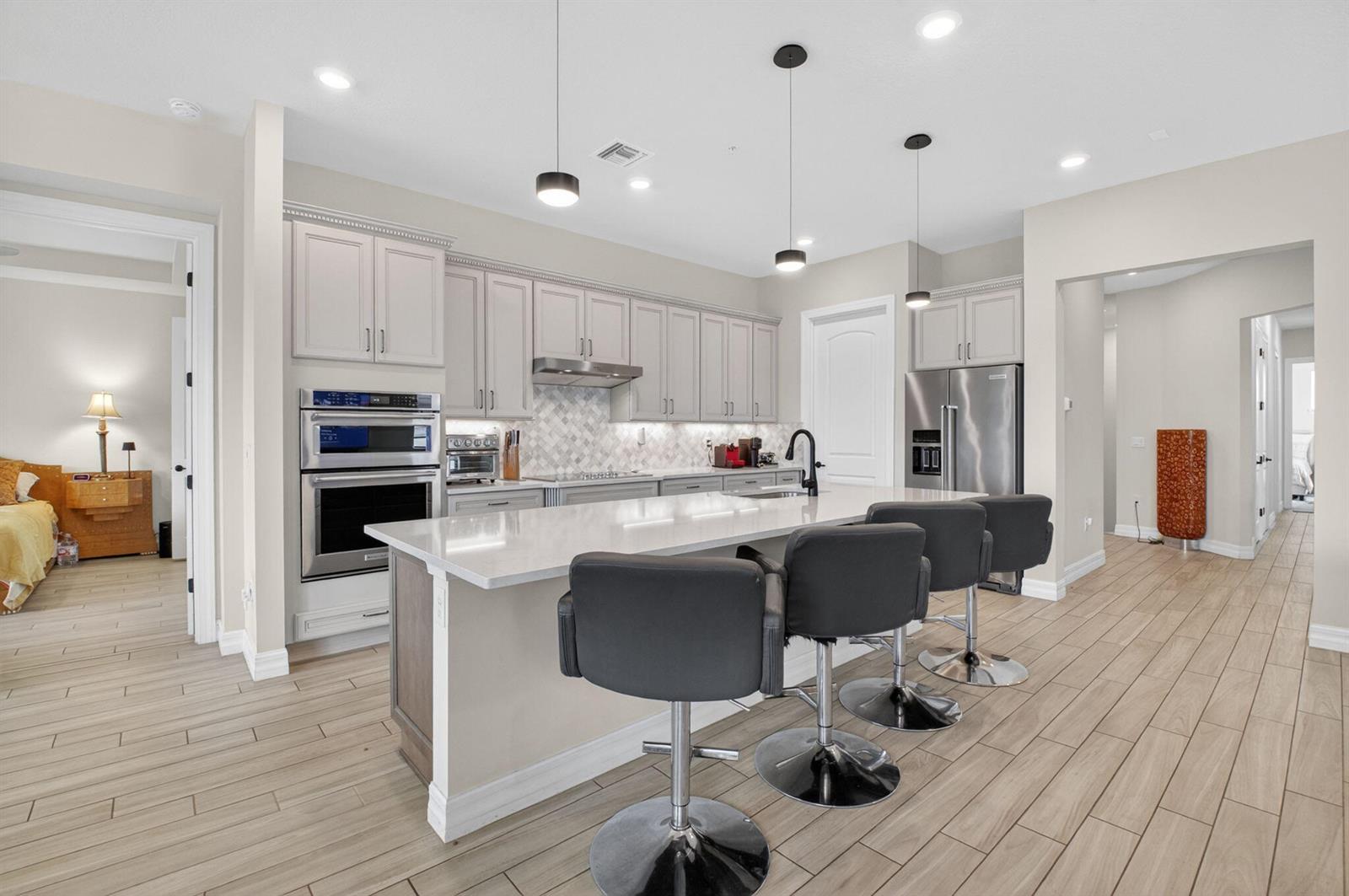 A modern kitchen features light gray cabinets, a white quartz island, and four bar stools — 21956 Canadensis Circle # 201, Boca Raton FL 33428, BOCA RATON, FL