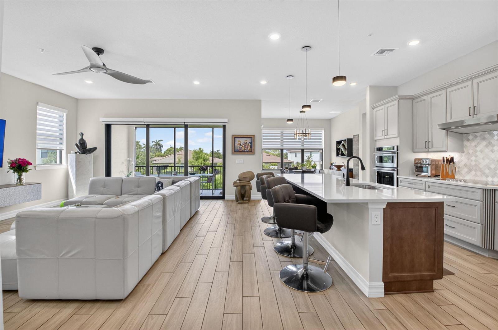 An open-concept living room and kitchen featuring a large sectional, island seating, and tile flooring — 21956 Canadensis Circle # 201, Boca Raton FL 33428, BOCA RATON, FL