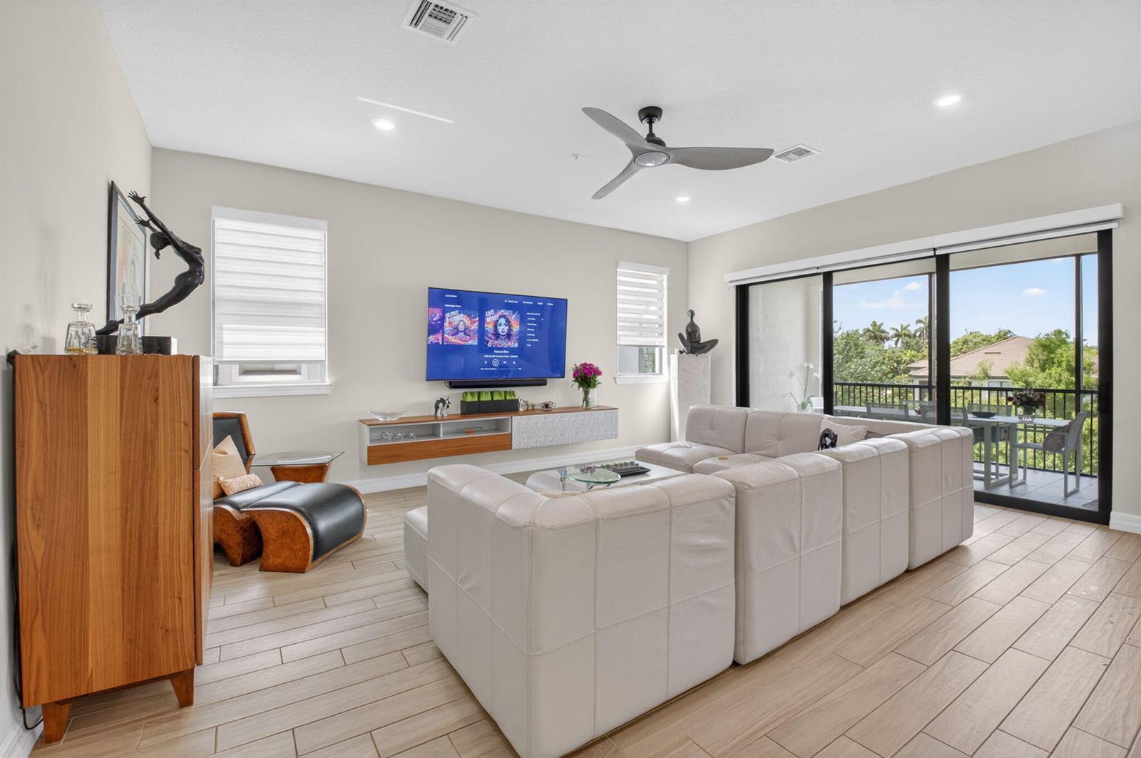 A modern living room features a large sectional sofa, wall-mounted television, and sliding glass doors — 21956 Canadensis Circle # 201, Boca Raton FL 33428, BOCA RATON, FL