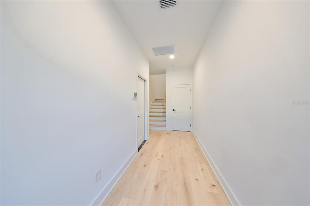 A hallway with light wood flooring leads to a staircase and two closed white doors — 4324 W GRAY STREET UNIT 3, TAMPA, FL