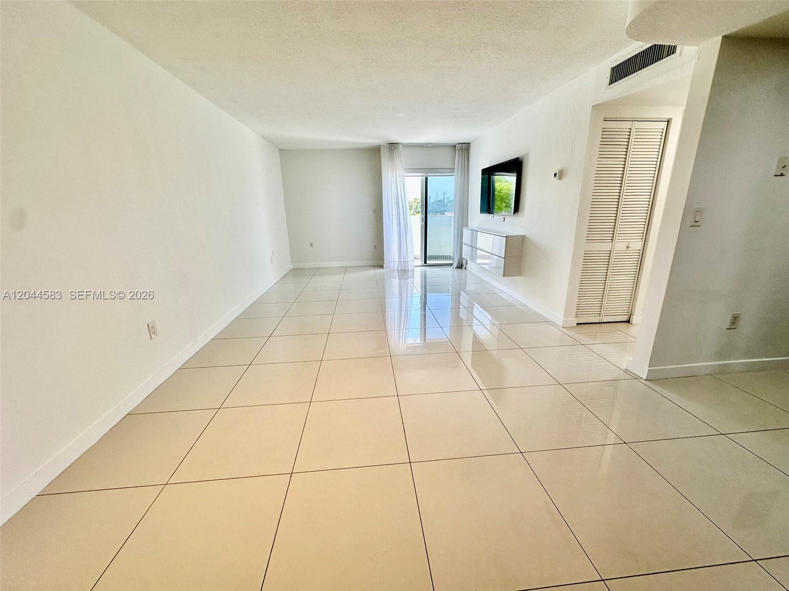 A bright, empty living room features large white floor tiles and a sliding glass door — 411 SW 37th Ave # 3D, Miami FL 33135, MIAMI, FL