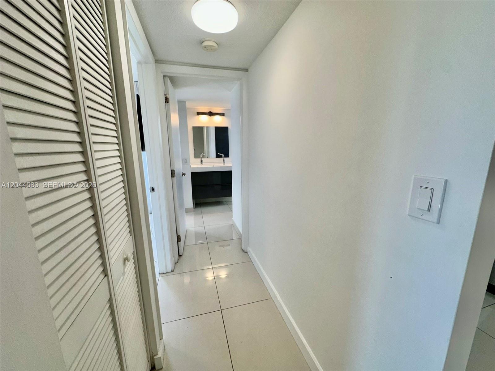 A hallway with white walls and tile flooring leads to a bathroom with a vanity — 411 SW 37th Ave # 3D, Miami FL 33135, MIAMI, FL