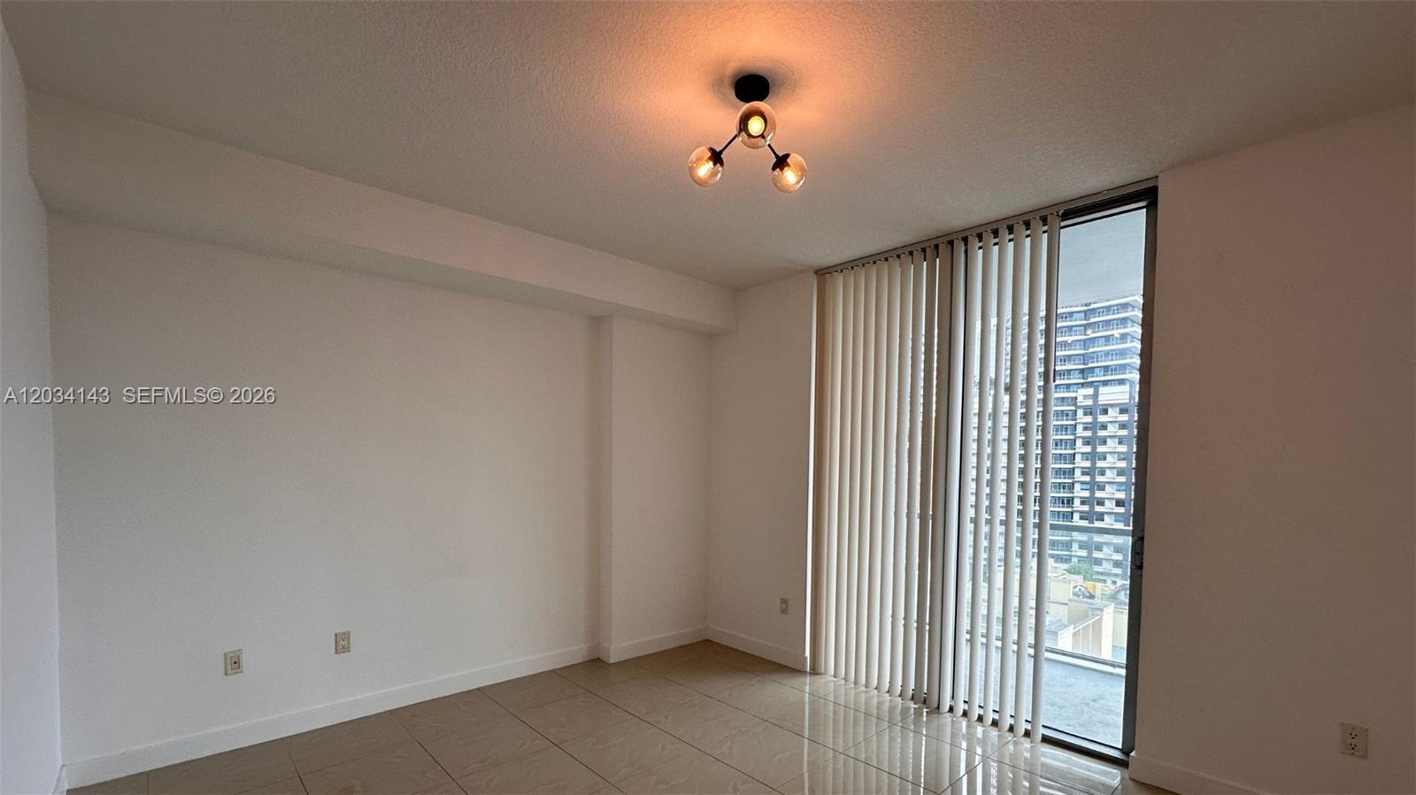 An empty room features light-colored tile flooring, a modern light fixture, and vertical window blinds — 79 SW 12th St, Miami FL 33130, MIAMI, FL