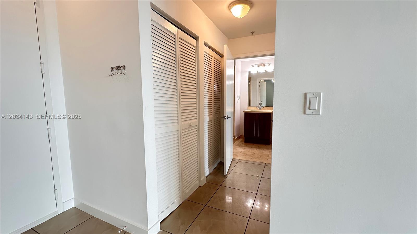 A hallway with louvered closet doors leads to a bathroom with tile flooring — 79 SW 12th St, Miami FL 33130, MIAMI, FL