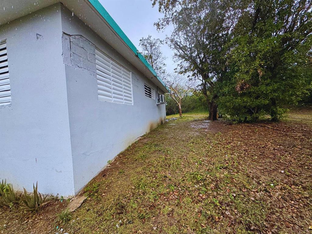 The exterior side of a light-colored concrete house features louvered windows and a small air conditioner — Calle #10 COMM MONTE SANTO P-2, VIEQUES, PR