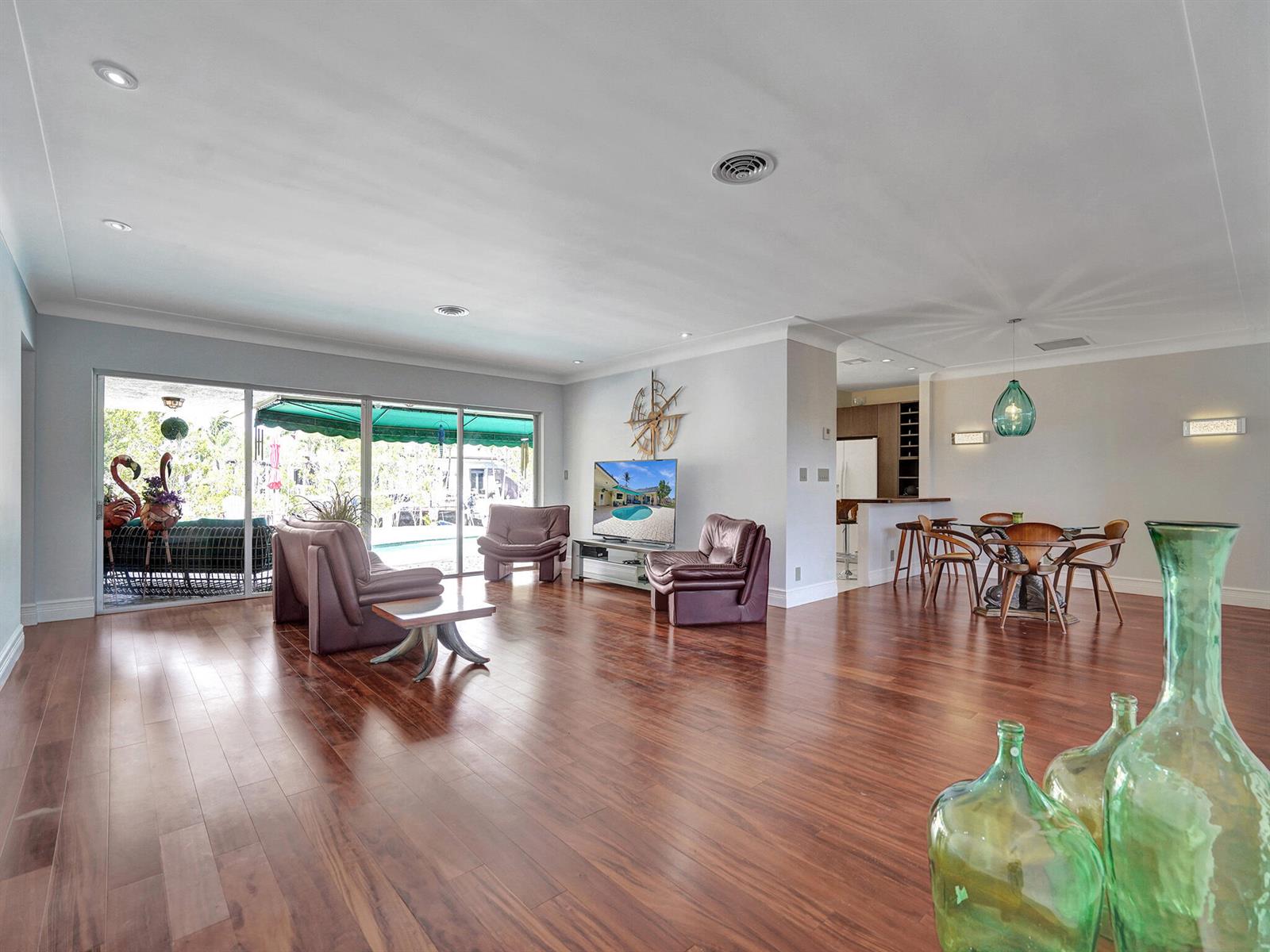 A spacious living and dining area with hardwood floors, glass sliding doors, and modern furniture — 3811 NE 26th Avenue, Lighthouse Point FL 33064, LIGHTHOUSE POINT, FL