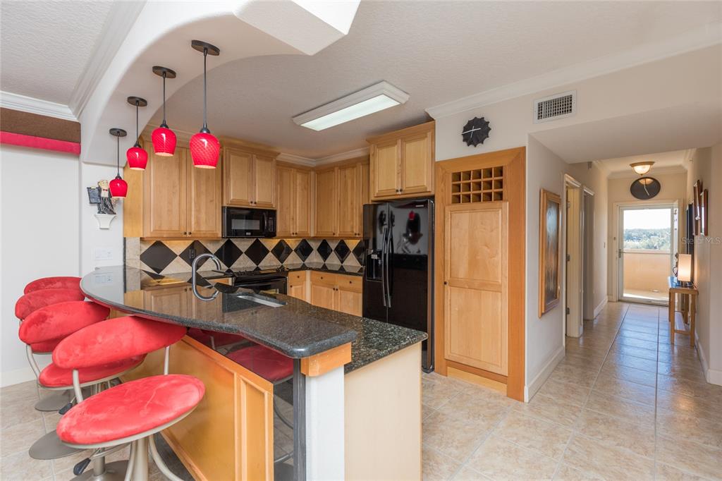 A kitchen with light wood cabinets, black granite countertops, red bar stools, and tiled floors — 80 SURFVIEW DRIVE UNIT 103, PALM COAST, FL