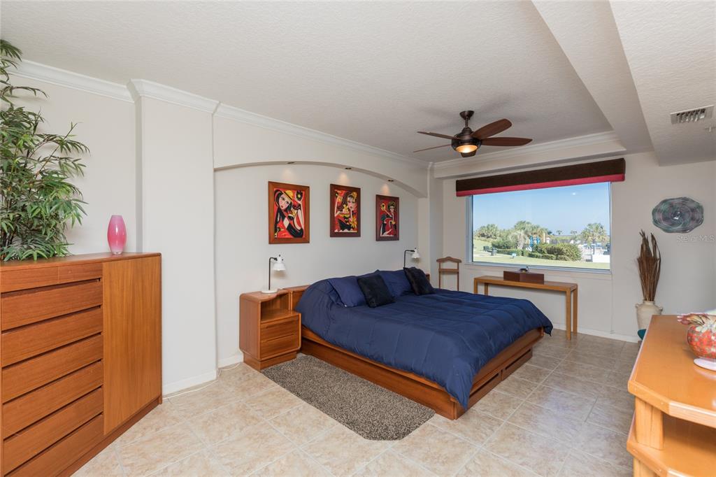 A bedroom features a platform bed, tile flooring, a ceiling fan, and a large window — 80 SURFVIEW DRIVE UNIT 103, PALM COAST, FL