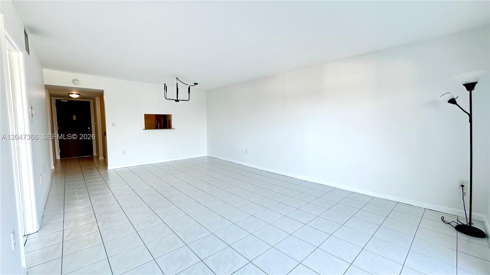 An empty room features white walls, light-colored tile flooring, a ceiling light fixture, and a floor lamp — 130 S Shore Dr # 4B, Miami Beach FL 33141, MIAMI BEACH, FL