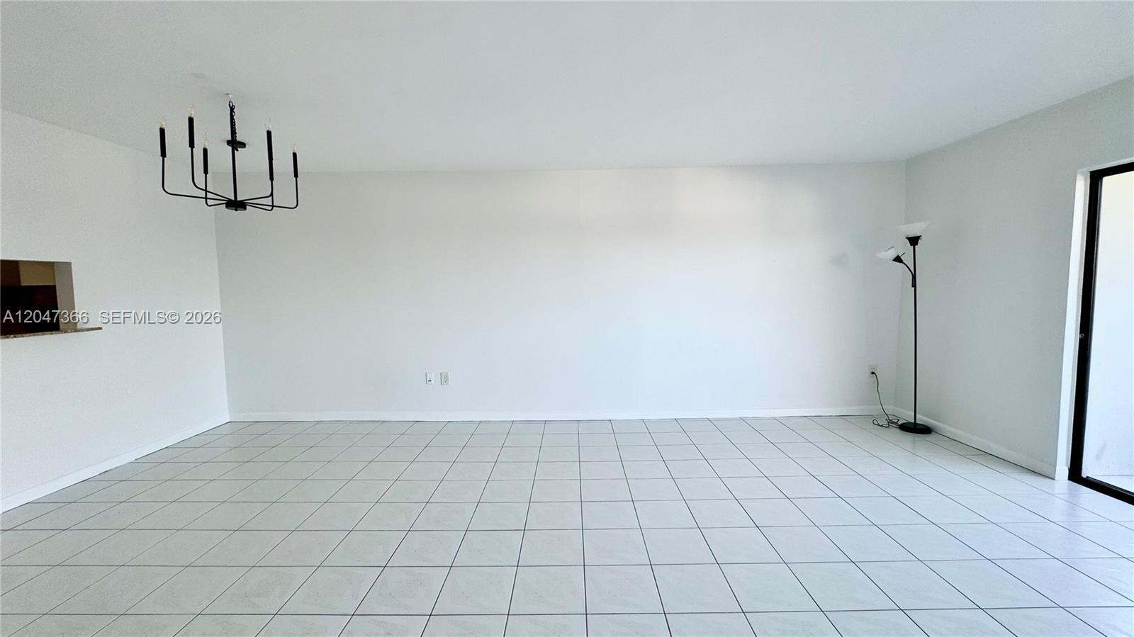 An empty room features white walls, light-colored tile flooring, a black chandelier, and a floor lamp — 130 S Shore Dr # 4B, Miami Beach FL 33141, MIAMI BEACH, FL