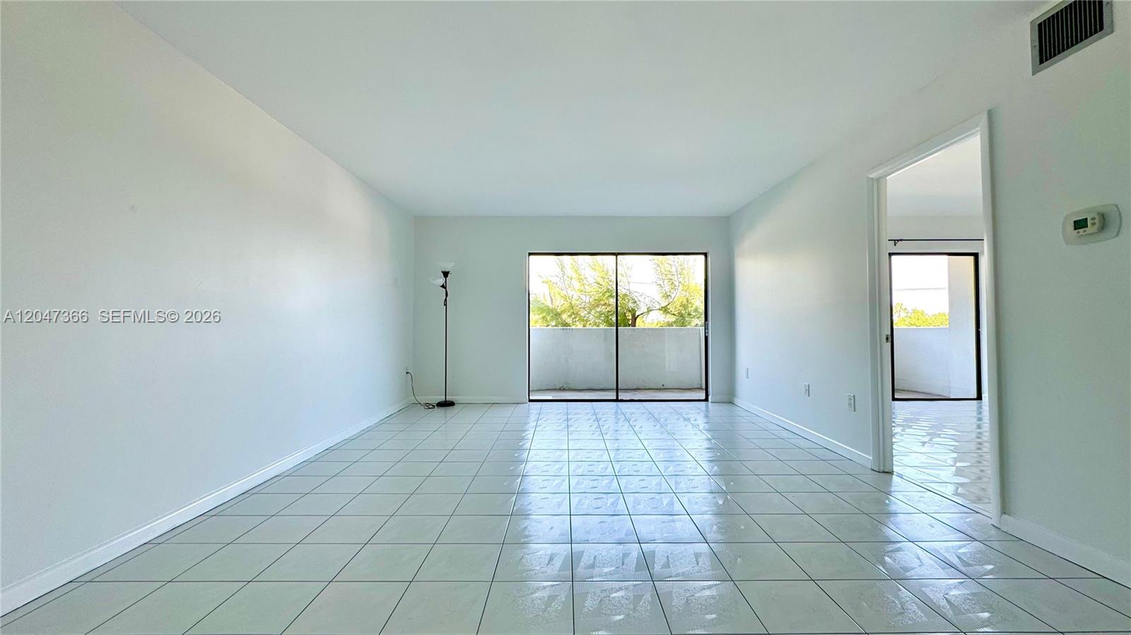 An empty room with light-colored tile flooring, white walls, and a sliding glass door — 130 S Shore Dr # 4B, Miami Beach FL 33141, MIAMI BEACH, FL