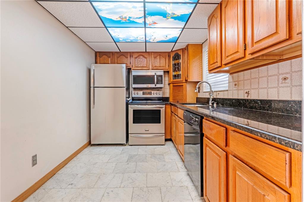A kitchen with wood cabinets, stainless steel appliances, dark countertops, and a decorative ceiling panel — 100 SILVER BEACH AVENUE UNIT 816, DAYTONA BEACH, FL